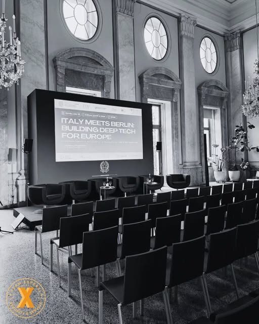 Leinwand mit Titel „Italy meets Berlin: Building Deep Tech for Europe“ in einem historischen Festsaal