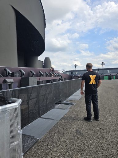 Mann mit schwarzem Shirt steht vor einer Tribüne und blickt in die Ferne.