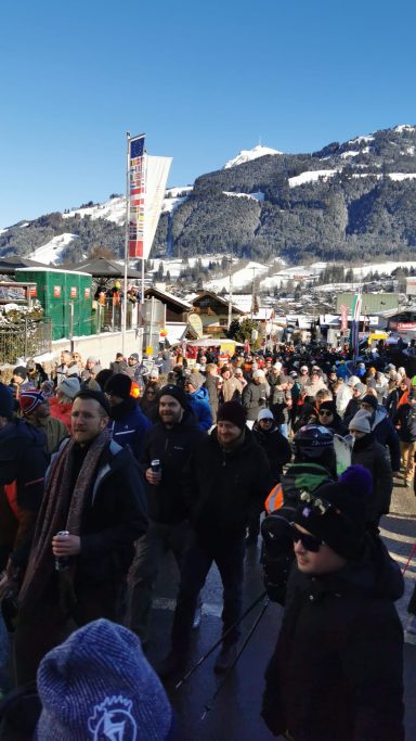 Menschenmenge auf einem Skigelände mit Bergsicht und klarem Himmel.