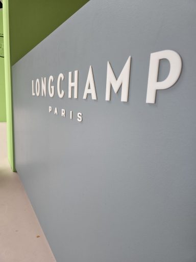 Weißer Schriftzug "LONGCHAMP" und "PARIS" auf grauem Hintergrund. Sicherheitsdienst